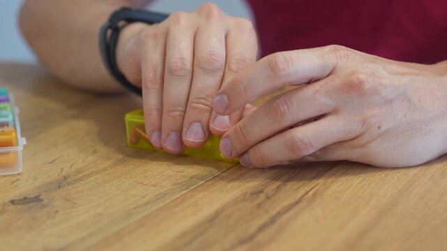The man opens the pillbox and takes the right pill
