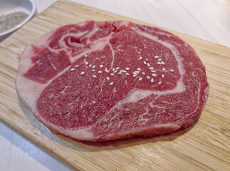 A close-up of a fresh, bright red raw ribeye steak with beautiful white marbling and a sprinkle of sesame seeds