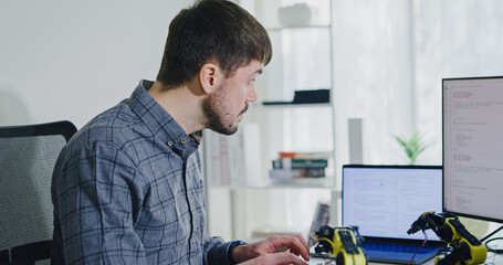 Young adult male freelance developer typing write prompt AI bot app program nomad terminal with coding at office. Artificial intelligence dashboard, robotics, user interface, machine learning concept.