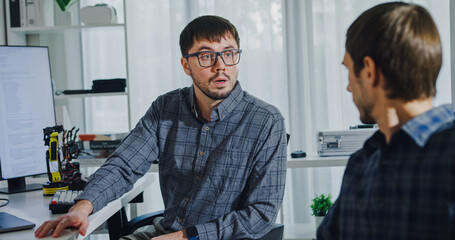 Adult male engineer team discusses AI software development robotic hand project use AI code solutions at tech workspace. Artificial intelligence interface, collaboration support prototype development.