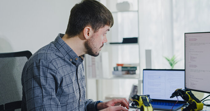 Young adult male freelance developer typing write prompt AI bot app program nomad terminal with coding at office. Artificial intelligence dashboard, robotics, user interface, machine learning concept.