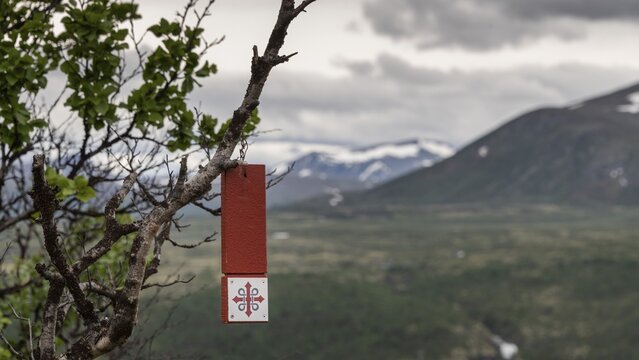 Wegmarkierung in Form eines rot-wei&szlig;en Schildes h&auml;ngt an einem Ast, Olavskreuz f&uuml;r Pilger, im Hintergrund Berge und Wolken, Olavsweg, Olavsleden oder Pilgrimsleden, Dovrefjell, Norwegen