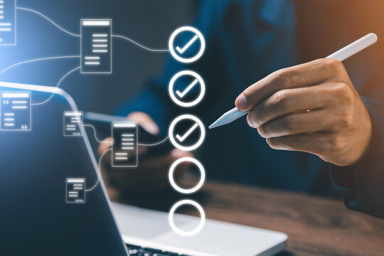 Hand holding a digital pen marking items on a virtual checklist connected to laptop, symbolizing project management, task organization, workflow process, and business productivity.