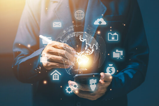Businessman holding smartphone with digital globe and futuristic icons, representing global communication, cloud technology, internet network, online business, and digital transformation.