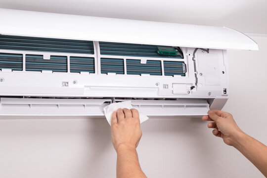 Close up of man cleaning air conditioner unit with a soft cloth. Concept of home maintenance, AC cleaning, dust removal, and indoor air care.