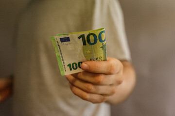Close-up of a person's hand holding a 100 euro banknote. Finance, economy, currency, money,...