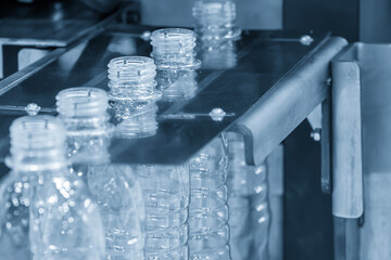 The  empty drinking water bottles  on the conveyor belt from blow mold machine in the light blue scene