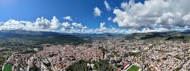 Fototapeta premium Aerial drone footage of L’Aquila, Italy, showcasing historic architecture, vibrant streets, and the stunning surrounding mountains