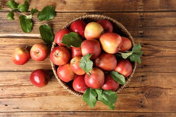Fresh ripe apples with green leaves in wicker basket on wooden table, top view