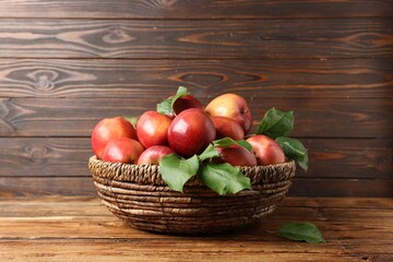 Fresh ripe apples with green leaves in wicker basket on wooden table