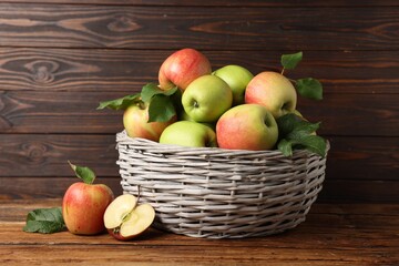 Fresh ripe apples with green leaves in wicker basket on wooden table