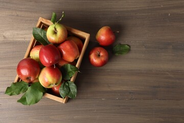 Fresh ripe apples with green leaves in crate on wooden table, top view. Space for text