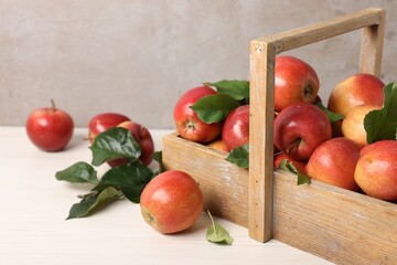 Fresh ripe apples with green leaves in crate on white wooden table, closeup