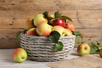 Fresh ripe apples with green leaves in wicker basket on white wooden table
