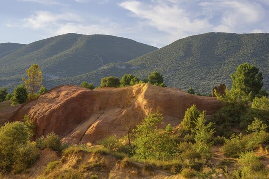 Ochre rock Colorado de Rustrel and wooded hills in the background, Rustrel, D&eacute;partement Vaucluse, France
