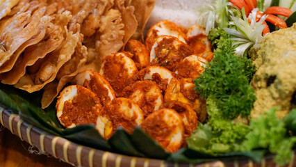 Indonesian traditional spicy boiled eggs known as telur balado, served with crispy rempeyek crackers and fresh vegetable garnish on a bamboo plate lined with banana leaves