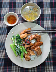 Traditional Vietnamese vegetarian dish with rice, soy meat, green vegetables, soup, and chili sauce served on a checkered tablecloth