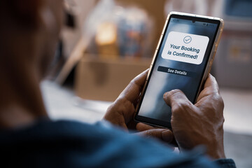 Man using smartphone displaying Your Booking is Confirmed notification on display. Flight or hotel or online appointment booking confirmation message. Selective focus.