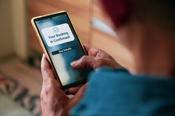 A South Asian man holding phone with Your booking is confirmed notification display. Selective focus on the text.