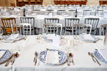 Formal dinning setup of chairs, long tables with tablecloths, plates, cutlery and glasses. Wide angle, interior setting, top down, no people