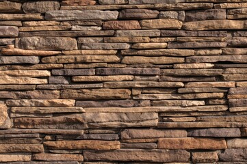 Natural stone wall featuring various stone sizes; Rustic stone cladding in earthy brown and beige tones
