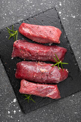 Raw beef steak. Raw fresh farm steak on black board on dark grey background. Raw beef steak for cooking vertical photo