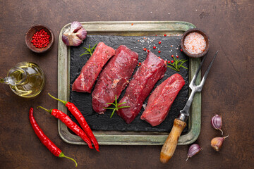 Raw beef steak. Raw fresh farm steak with rosemary, salt and pepper on black board on dark background. Raw beef steak and spices for cooking top view