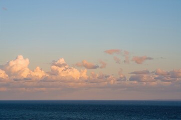 Obraz premium Evening sun setting above a vast azure ocean and cloudy sky, highlighting a scenic natural view.