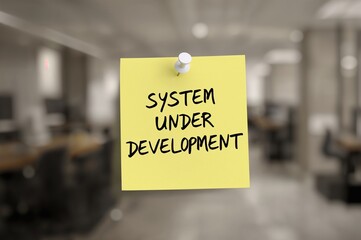 Yellow paper note pinned on corkboard with white thumbtack displaying 'System Under Development', copy space included