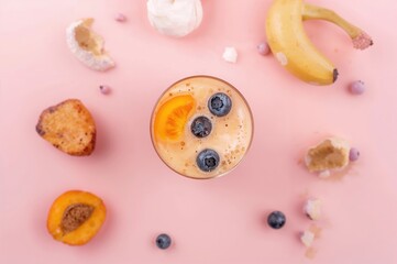 A creamy blend of apricot, banana, and blueberry with milk set against a pastel pink backdrop. Overhead view. Contemporary and sleek summer theme.