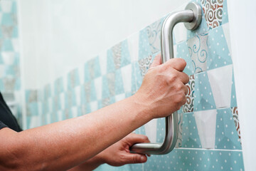 Asian woman patient use toilet support rail in bathroom, handrail safety grab bar, security in nursing hospital.