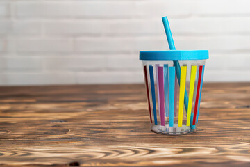 Playful Sipping Fun A Colorful Striped Cup with a Blue Lid and Straw on a Rustic Wooden Table Surface