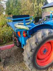 Close-up of a vintage blue tractor with a trailer and a giant marrow/squash. Autumn harvest, agriculture, garden machinery.