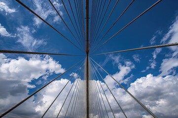 Fototapeta premium White metal framework and steel cables viewed from below against a clear blue sky. Diagonal structural elements and bridge features converging to a vanishing point.