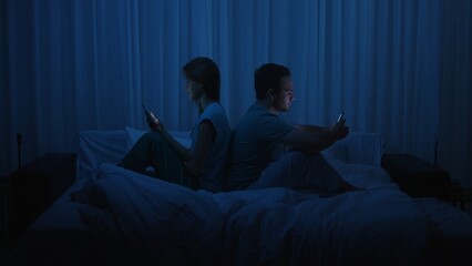 A couple sits back to back in bed at night using smartphones