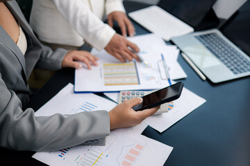 Businesswomen analyzing financial data using smartphone and laptop in modern office