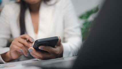 Businesswoman using smartphone for digital communication and online financial work in modern office