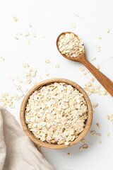 Rolled oats or oat flakes in a wooden bowl on white background.