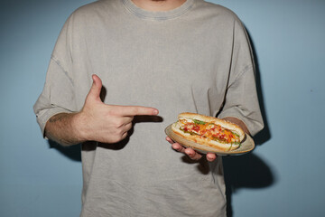 Caucasian young adult man holding plate with sandwich and pointing at food, standing against plain...