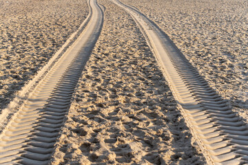 Fresh tire tracks in the sand form striking parallel lines leading into the distance. The light creates strong shadows and textures.