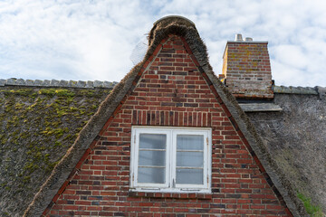 A red-brick gable house with a thatched roof and white-framed windows. The rustic design is enhanced by a brick chimney.