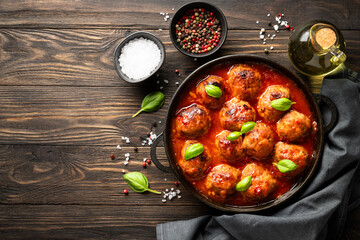 Meatballs in tomato sauce with basil leaves on wooden table.