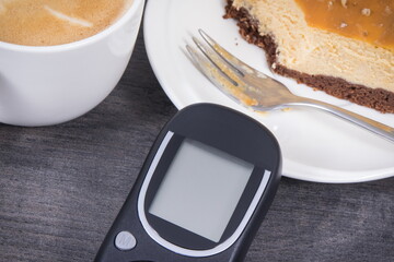 Glucose meter, sweet cheesecake and cup of coffee with milk. Measuring and sugar level control during diabetes