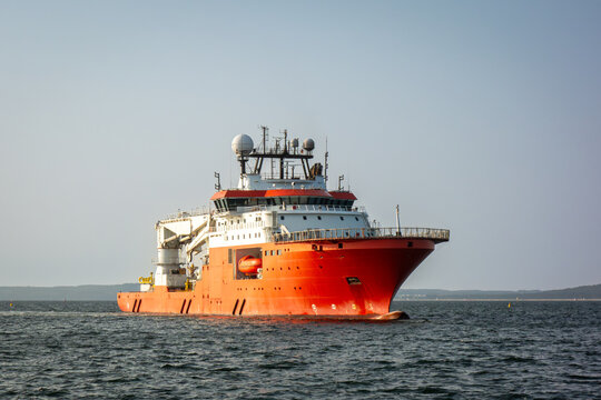 Modern offshore support vessel. Large red industrial ship with crane and lifeboat. Maritime transport and logistics for the oil and gas energy industry.