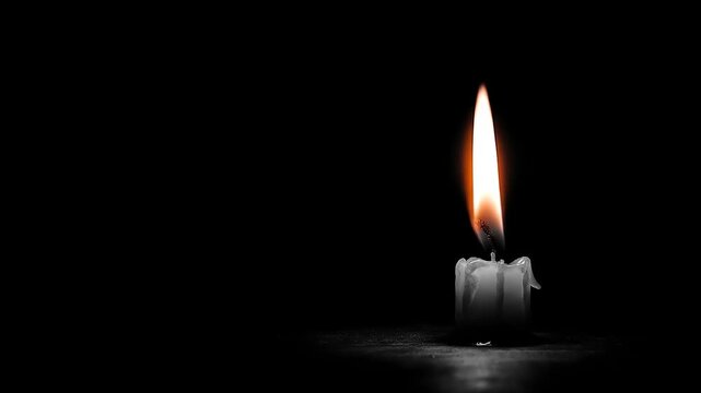 Burning candle in darkness with warm flame and melting wax on black background