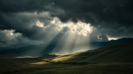 Sun rays piercing through dark clouds illuminating a grassy landscape with distant mountains