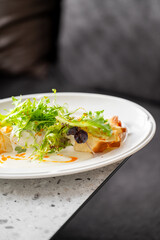 Gourmet savory tart topped with fresh frisée and baby greens, drizzled with creamy and orange sauces, served on a ceramic plate in a casual home dining setting