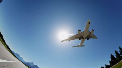 Passenger airplane landing on airport runway, framed by majestic mountain landscape and lush forest, under vivid blue sky and bright sunlight - Powered by Adobe