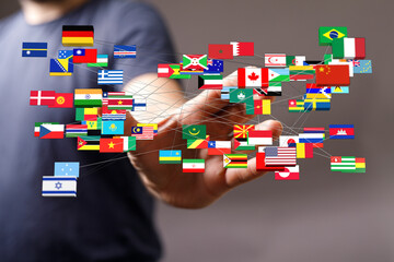 Image depicts a human hand connected to flags of various countries, symbolizing globalization,...
