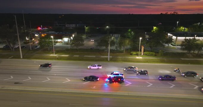 Nighttime traffic stop on USA city street as police pull over speeding vehicle. Patrol car lights flash in urban traffic environment.